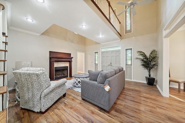 living room with a high ceiling, ceiling fan, crown molding, and hardwood / wood-style floors