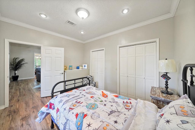 bedroom featuring hardwood / wood-style flooring, ornamental molding, a textured ceiling, and two closets