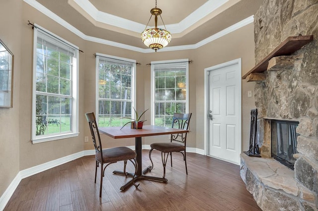 dining room with hardwood / wood-style flooring, a stone fireplace, ornamental molding, and a tray ceiling