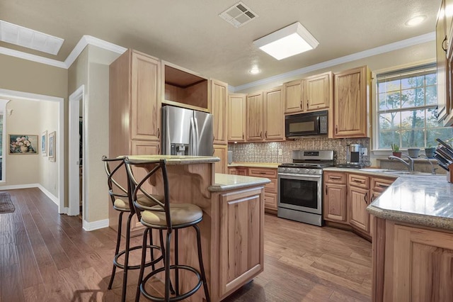 kitchen with light brown cabinetry, stainless steel appliances, hardwood / wood-style floors, a center island, and a breakfast bar area