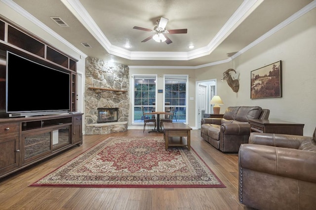 living room with a tray ceiling, ceiling fan, and light wood-type flooring