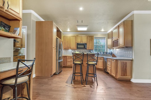 kitchen featuring hardwood / wood-style floors, ornamental molding, a breakfast bar area, and appliances with stainless steel finishes