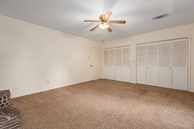 unfurnished bedroom with ceiling fan, carpet floors, two closets, and a textured ceiling