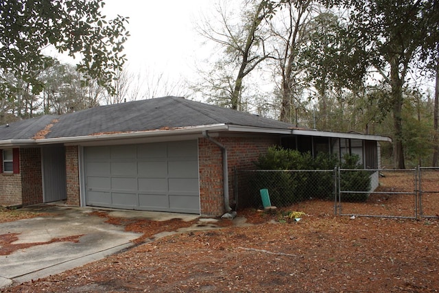 view of property exterior with brick siding, driveway, a garage, and fence