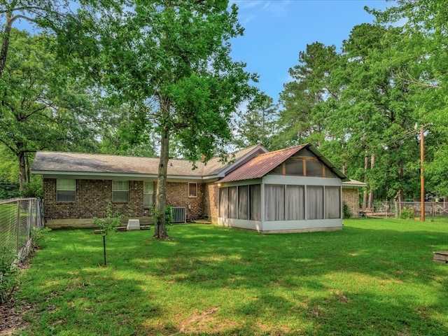 back of house featuring brick siding, a sunroom, central AC, a fenced backyard, and a yard