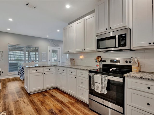 kitchen with white cabinets, appliances with stainless steel finishes, light wood-type flooring, and a peninsula