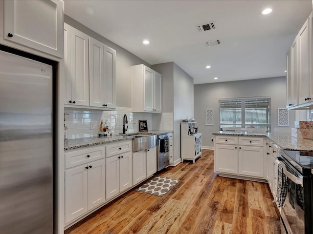 kitchen featuring backsplash, range with electric cooktop, light wood-type flooring, stainless steel fridge, and a sink