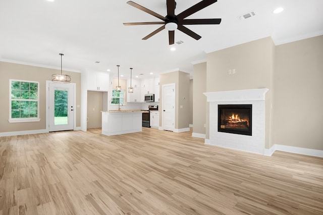 1911 Paul Ave, Lufkin, TX 75901 - unfurnished living room featuring ceiling fan, crown molding, a brick fireplace, light wood-style floors, and plenty of natural light