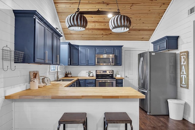 kitchen with butcher block countertops, stainless steel appliances, hanging light fixtures, and blue cabinetry