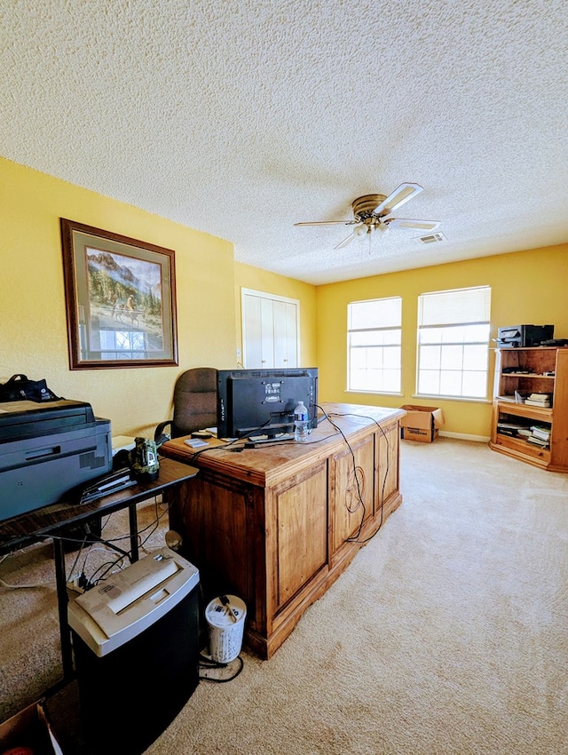 home office featuring light carpet, a textured ceiling, visible vents, and a ceiling fan