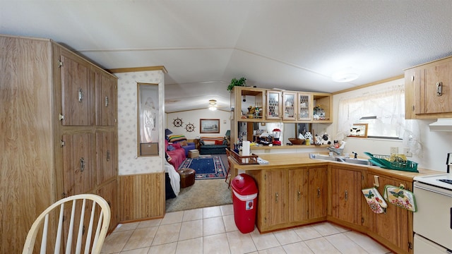 kitchen with sink, white range with electric cooktop, wood walls, kitchen peninsula, and light tile patterned floors