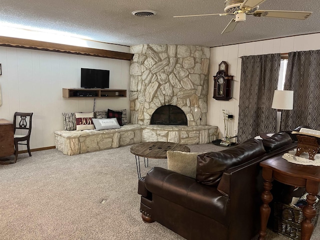 living room featuring ceiling fan, a stone fireplace, carpet floors, a textured ceiling, and wooden walls