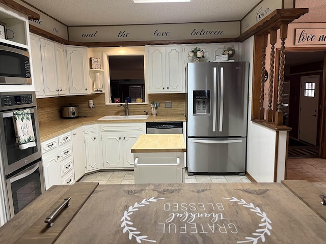 kitchen featuring tasteful backsplash, a textured ceiling, stainless steel appliances, sink, and white cabinets