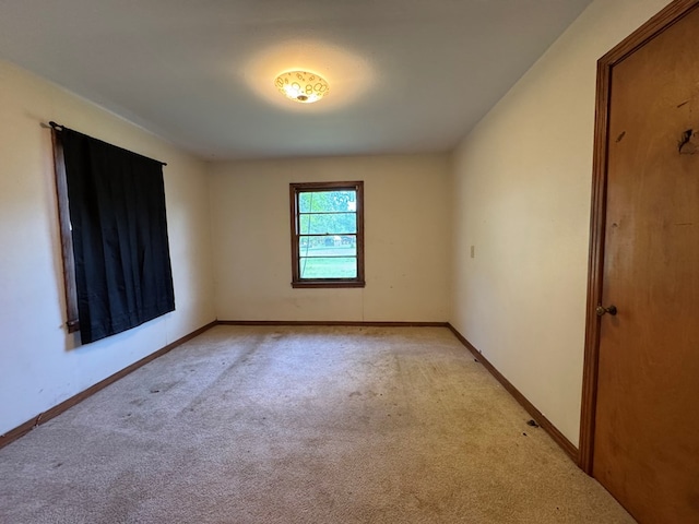 spare room featuring light colored carpet and baseboards