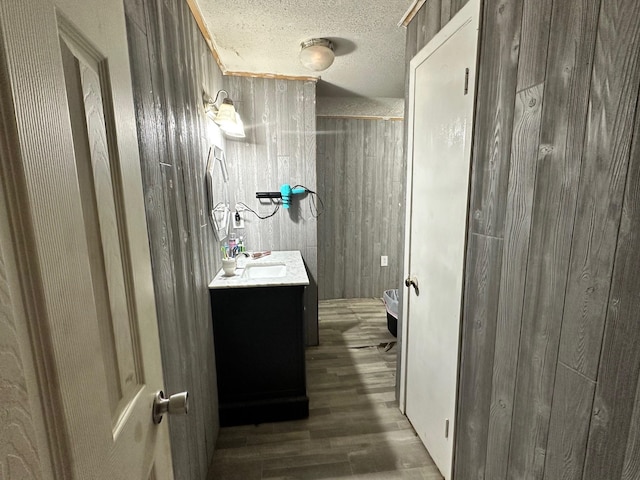 bathroom featuring a textured ceiling, vanity, wooden walls, and wood-type flooring