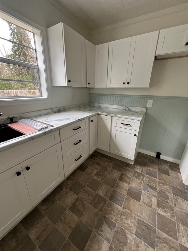 kitchen featuring a sink, light stone countertops, white cabinets, and wainscoting