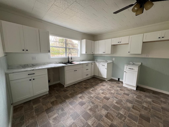 kitchen featuring white cabinetry, baseboards, a wainscoted wall, and a sink