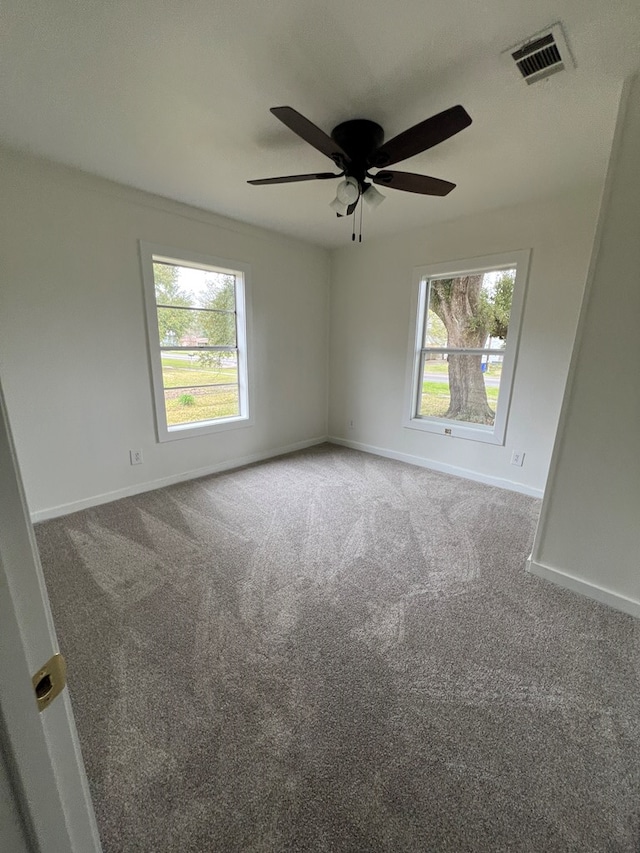 carpeted spare room featuring visible vents, baseboards, a healthy amount of sunlight, and ceiling fan