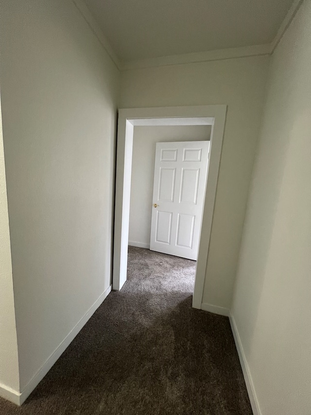 corridor featuring dark colored carpet, baseboards, and crown molding