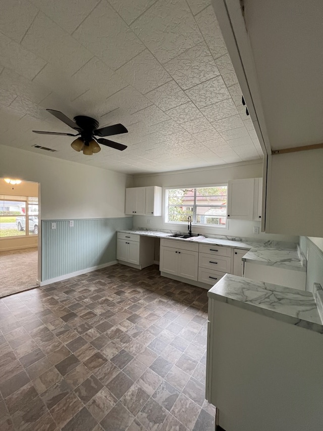 kitchen with light stone countertops, visible vents, a sink, white cabinets, and wainscoting