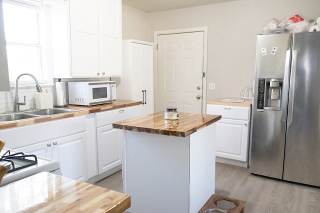 kitchen featuring white cabinets, stainless steel fridge with ice dispenser, white microwave, wooden counters, and a sink