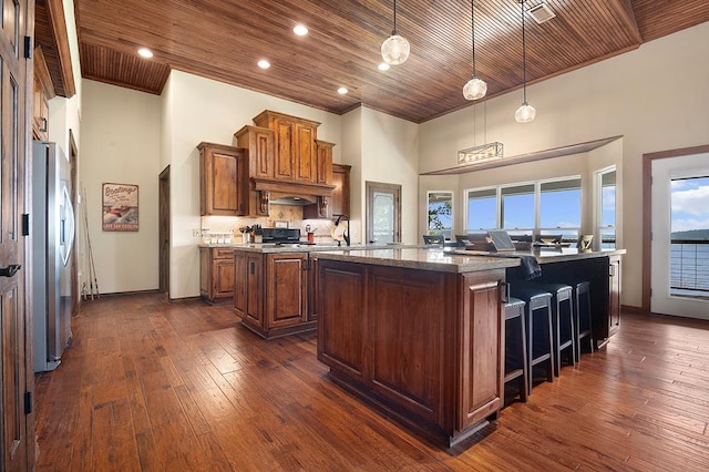 388 County Road 5597, Etoile, TX 75944 - kitchen with an island with sink, freestanding refrigerator, brown cabinets, dark wood-style flooring, and a kitchen breakfast bar