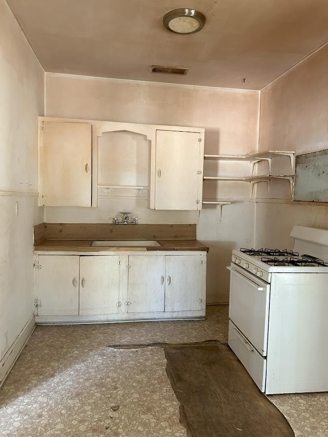 kitchen featuring white gas stove, white cabinetry, and sink