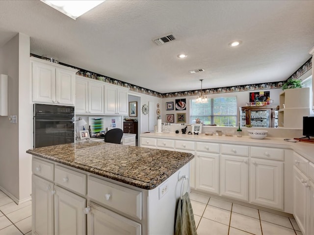 325 Evans Gann Rd, Lufkin, TX 75904 - kitchen with oven, a kitchen island, light tile patterned floors, white cabinetry, and dark stone counters