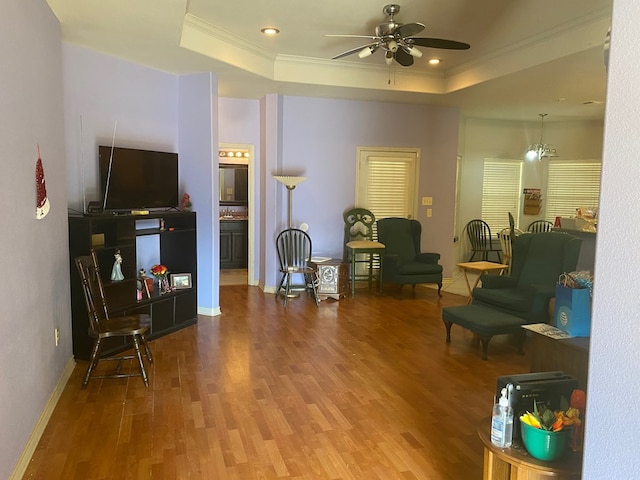 living room with hardwood / wood-style flooring, ceiling fan with notable chandelier, ornamental molding, and a tray ceiling