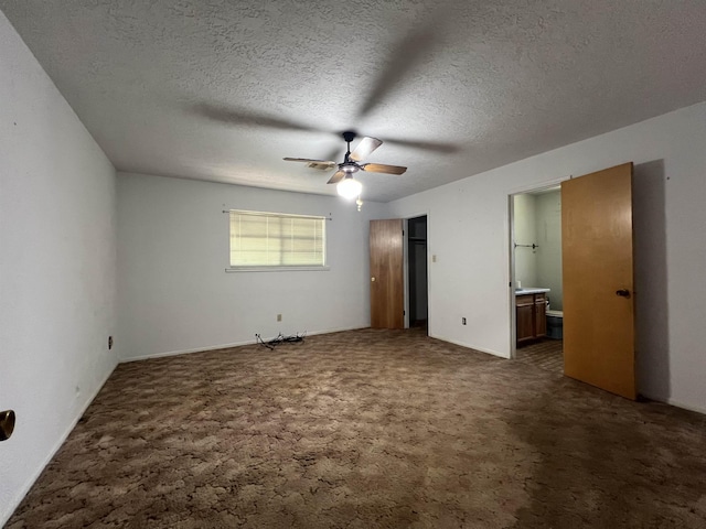 unfurnished bedroom featuring ensuite bath, ceiling fan, dark carpet, and a textured ceiling