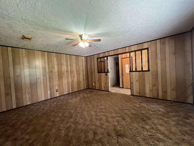 carpeted spare room featuring a textured ceiling and wooden walls