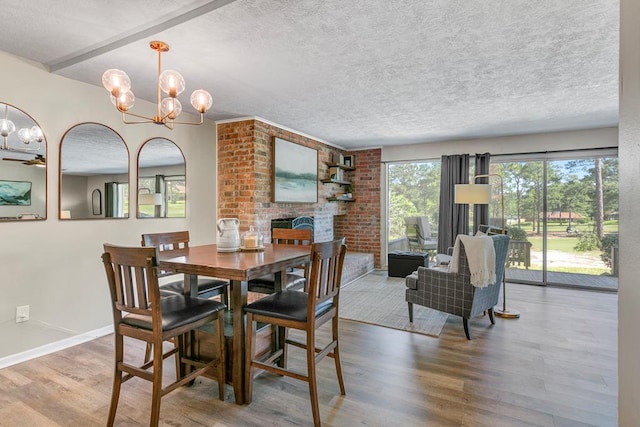 dining space with a textured ceiling, an inviting chandelier, wood-type flooring, and a brick fireplace