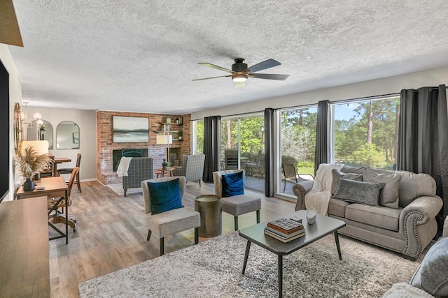 living room with a textured ceiling, a brick fireplace, light hardwood / wood-style floors, and ceiling fan