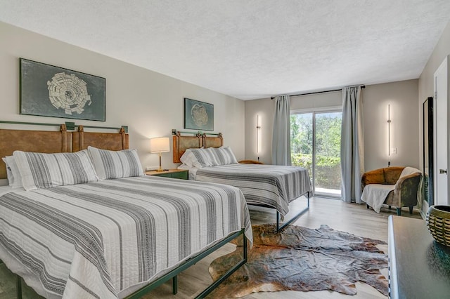 bedroom featuring access to outside, a textured ceiling, and light hardwood / wood-style flooring