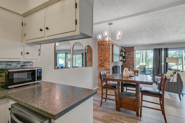 kitchen with a textured ceiling, white cabinetry, stainless steel appliances, light hardwood / wood-style floors, and a notable chandelier