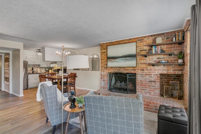 living room featuring a fireplace, a notable chandelier, a textured ceiling, and light hardwood / wood-style flooring