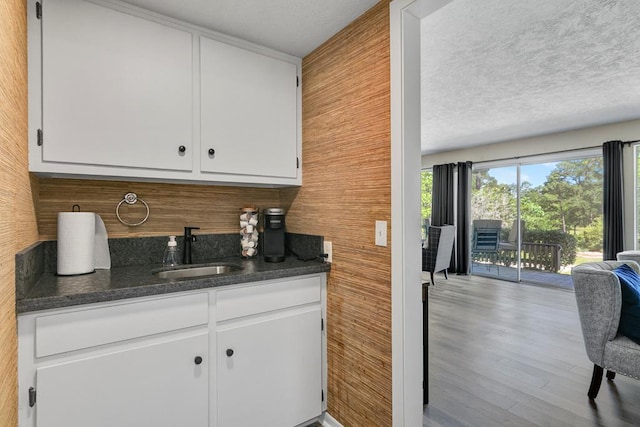 kitchen featuring sink, white cabinetry, dark stone counters, and wooden walls