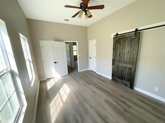 1515 County Road 826, Buna, TX 77612 - unfurnished bedroom with a barn door, baseboards, wood finished floors, and ceiling fan