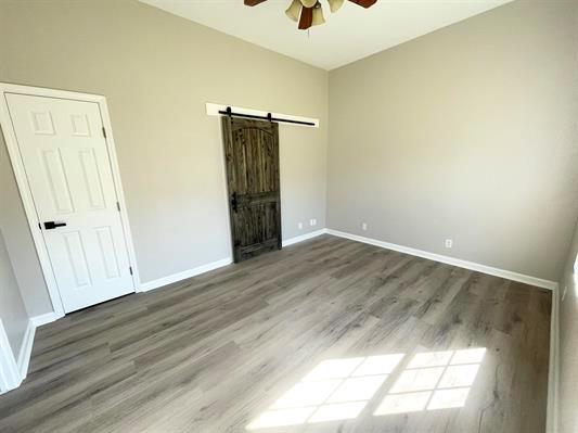 1515 County Road 826, Buna, TX 77612 - unfurnished bedroom with a barn door, wood finished floors, baseboards, and ceiling fan