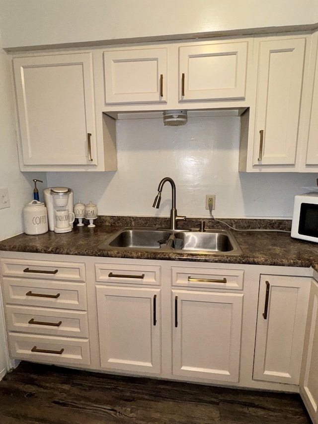 kitchen with dark countertops, white microwave, white cabinetry, and a sink