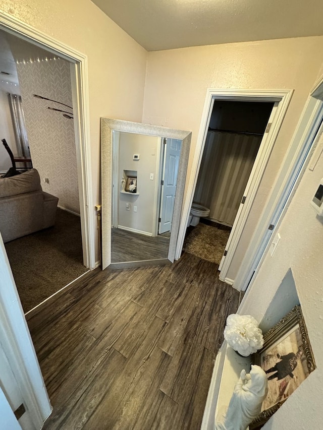 hall with dark wood-type flooring and a textured wall