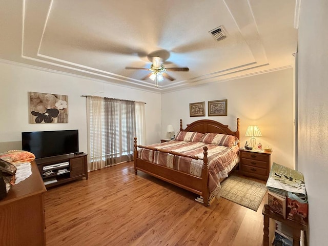 bedroom featuring a raised ceiling, ceiling fan, hardwood / wood-style floors, and crown molding