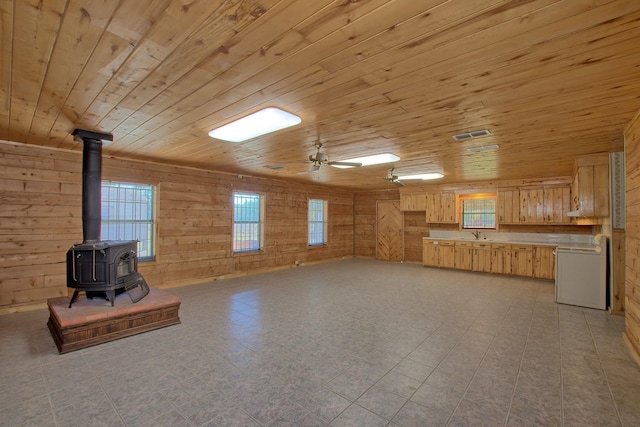 unfurnished living room with a wood stove, wood walls, wood ceiling, and ceiling fan