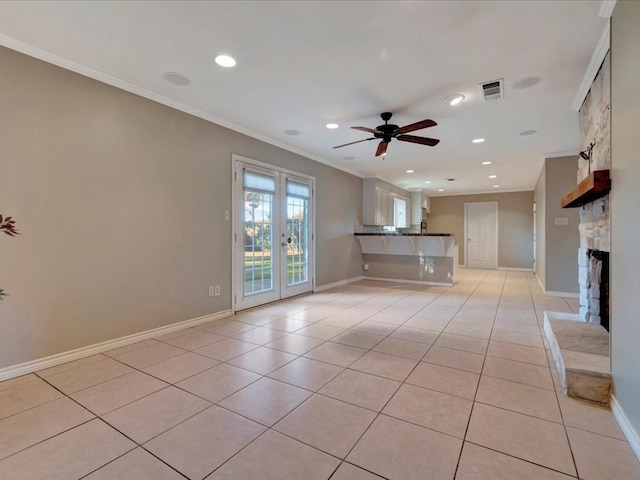 unfurnished living room with french doors, ornamental molding, ceiling fan, light tile patterned floors, and a stone fireplace