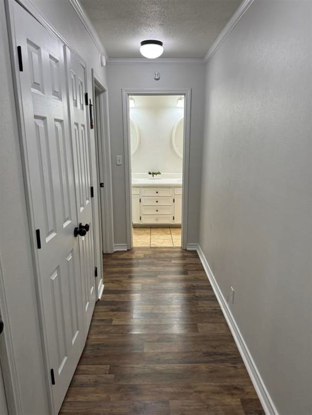 corridor featuring a textured ceiling, crown molding, and dark wood-type flooring