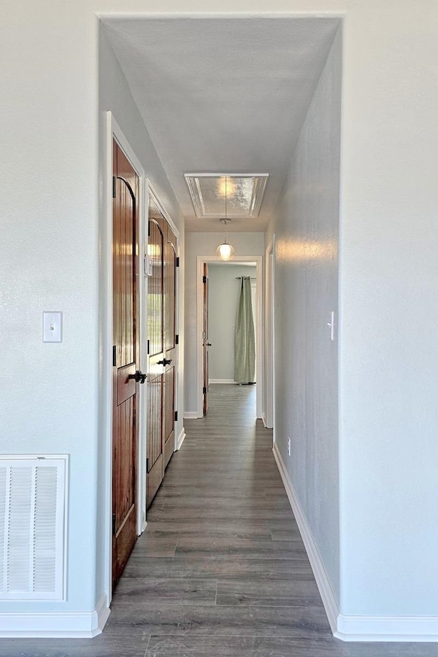 corridor with dark wood-type flooring, visible vents, baseboards, and attic access