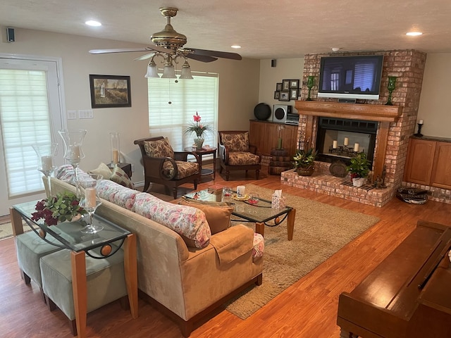 living room featuring hardwood / wood-style floors, a fireplace, ceiling fan, and a textured ceiling