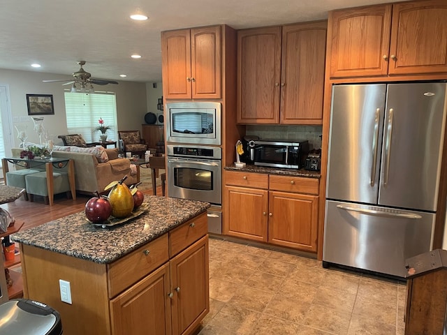 kitchen with ceiling fan, a center island, stainless steel appliances, dark stone counters, and decorative backsplash