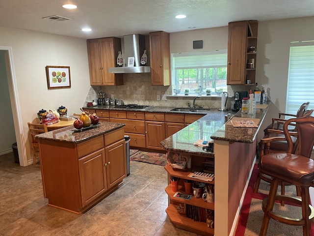 kitchen with decorative backsplash, wall chimney exhaust hood, sink, dark stone countertops, and a center island