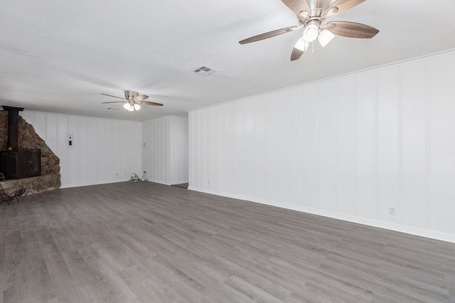 unfurnished living room featuring visible vents, ceiling fan, wood finished floors, and a wood stove